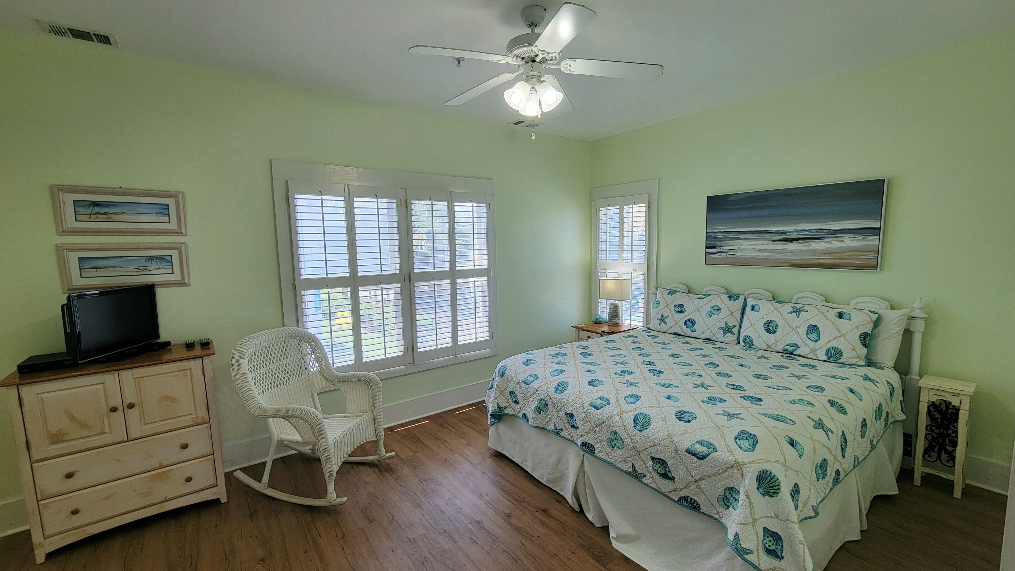 A bedroom with a bed, rocking chair, dresser, and a ceiling fan.