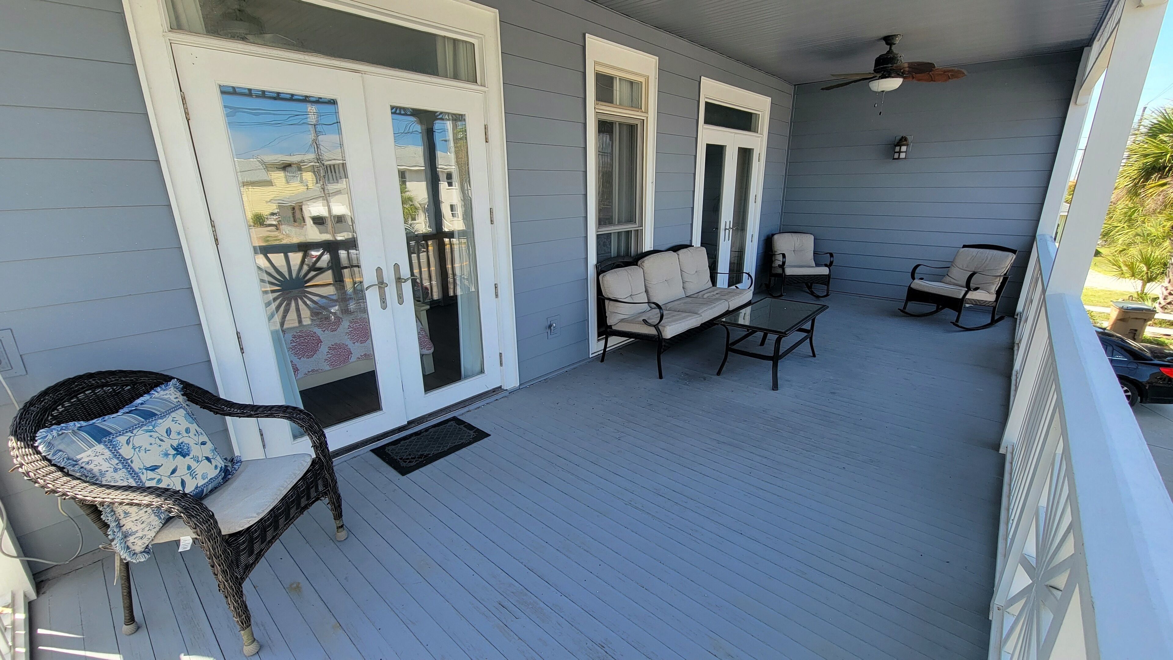 A covered porch with a wicker chair, a sofa, and a table.