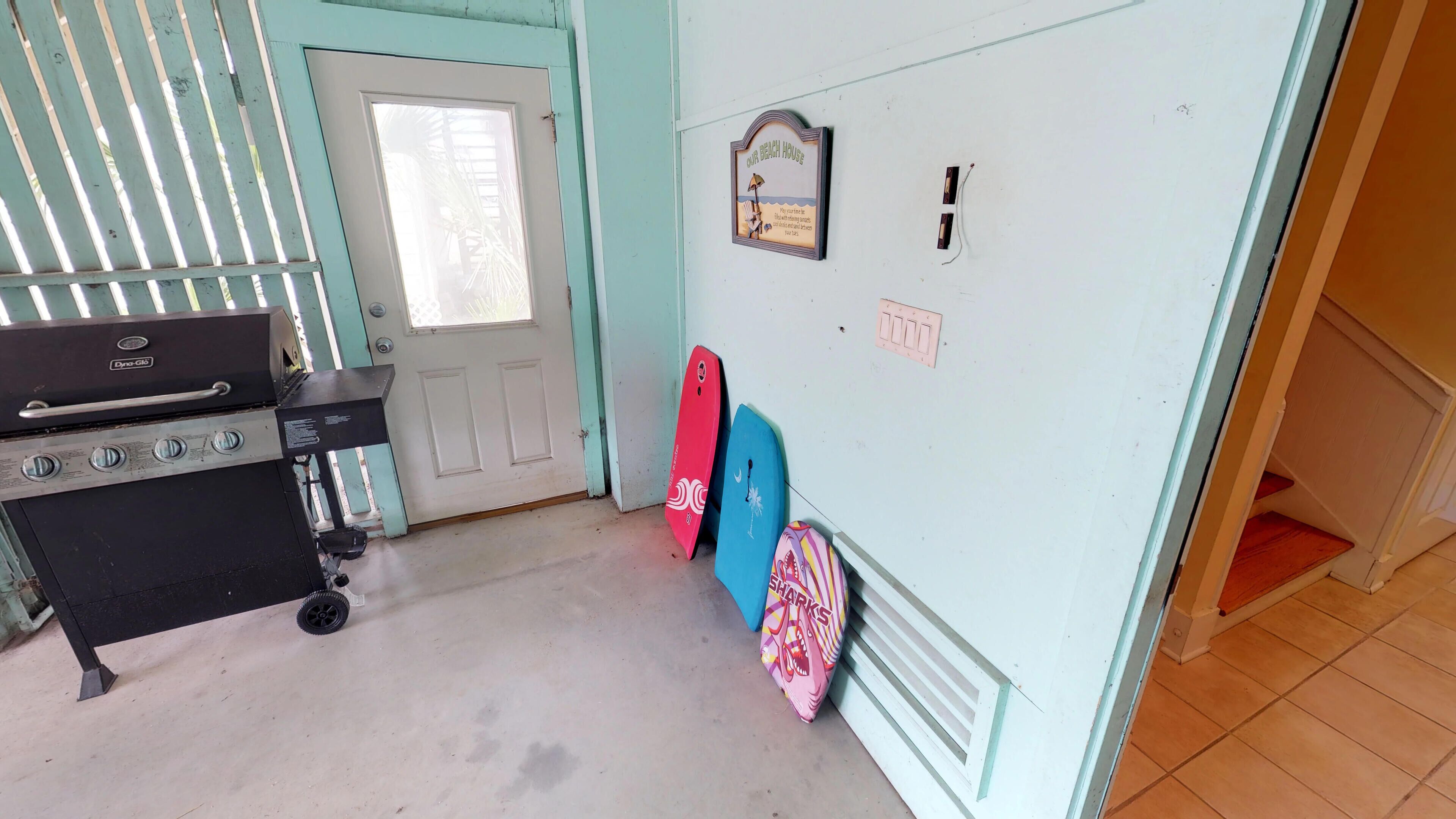 A kitchen with a grill, a door with a window, and surfboards against the wall.