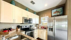 Una cocina moderna con gabinetes blancos, electrodomésticos de acero inoxidable, encimeras de granito y un refrigerador grande.