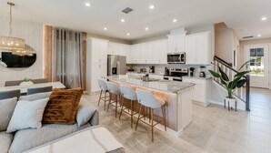 Una cocina moderna con armarios blancos, una isla central con taburetes y una zona de comedor con sofá y sillas.