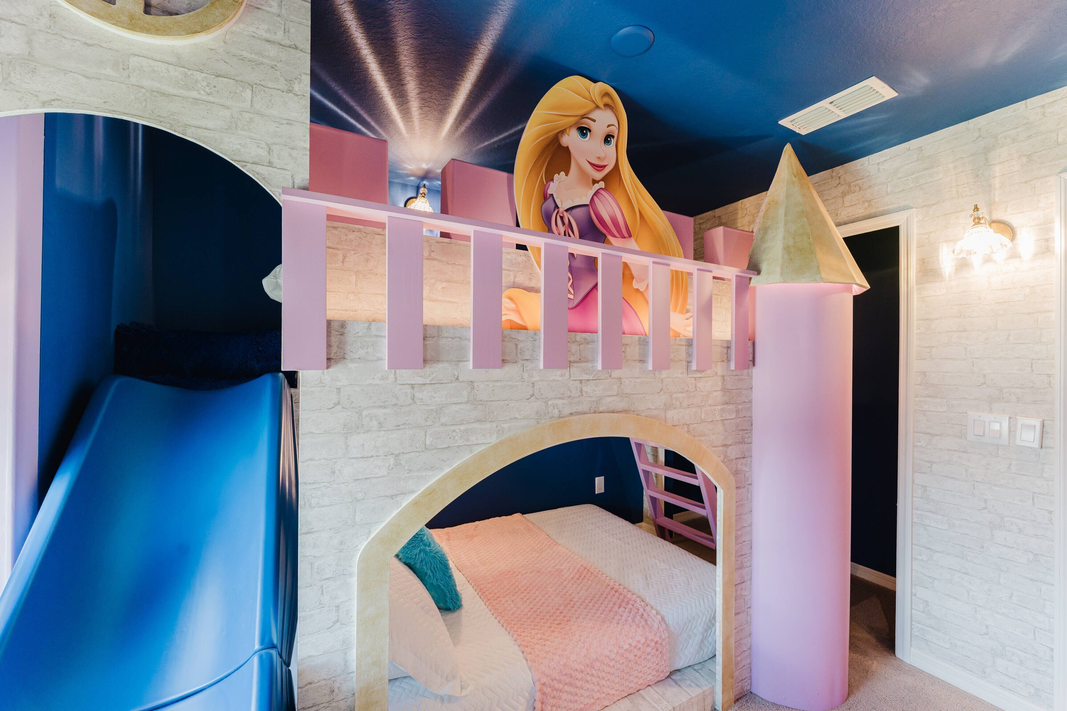 Een kinderspeelkamer met een glijbaan, een stapelbed en een muurschildering met een kasteelthema op het plafond.