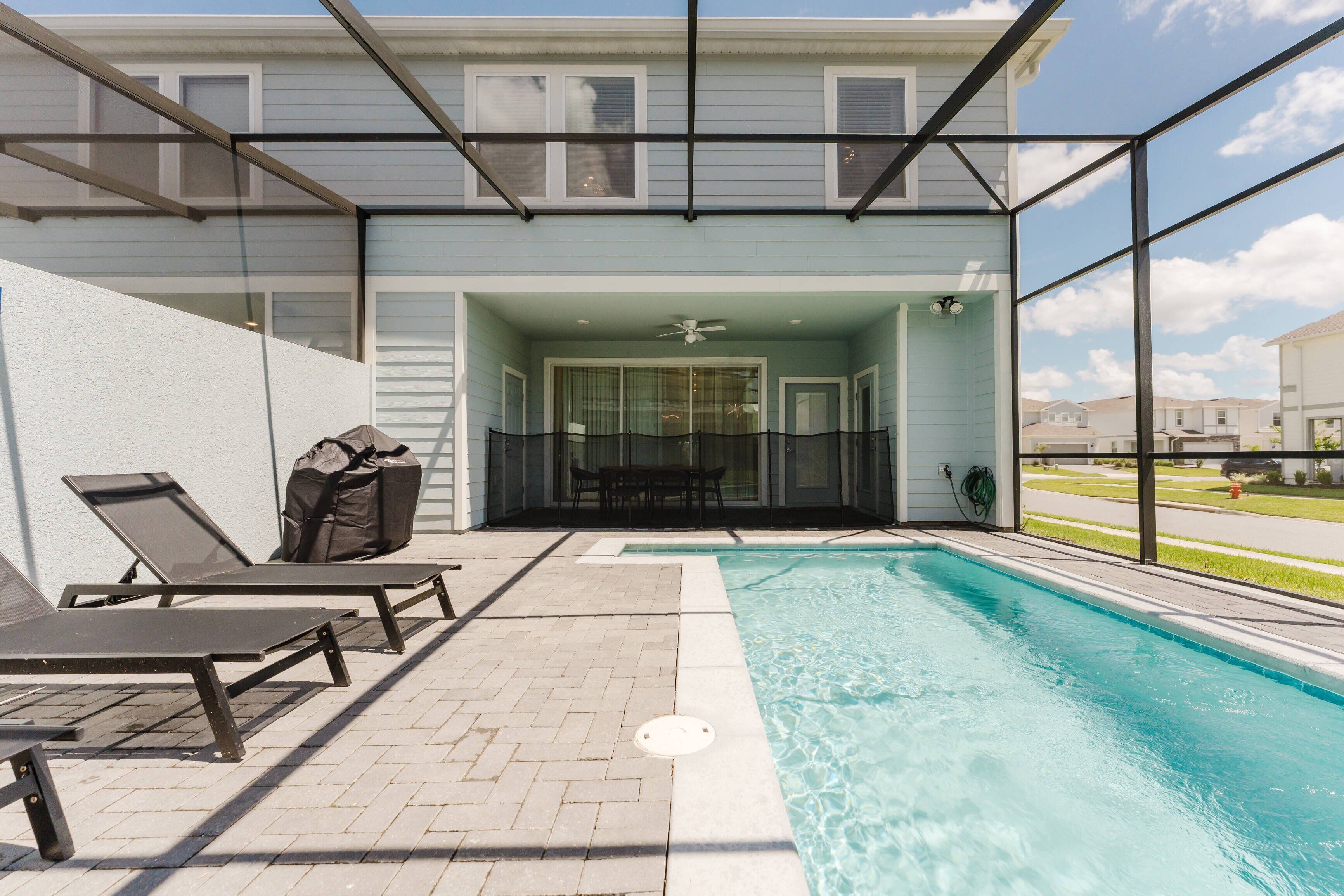 A pool area with lounge chairs, a covered seating area, and a view of the neighborhood.