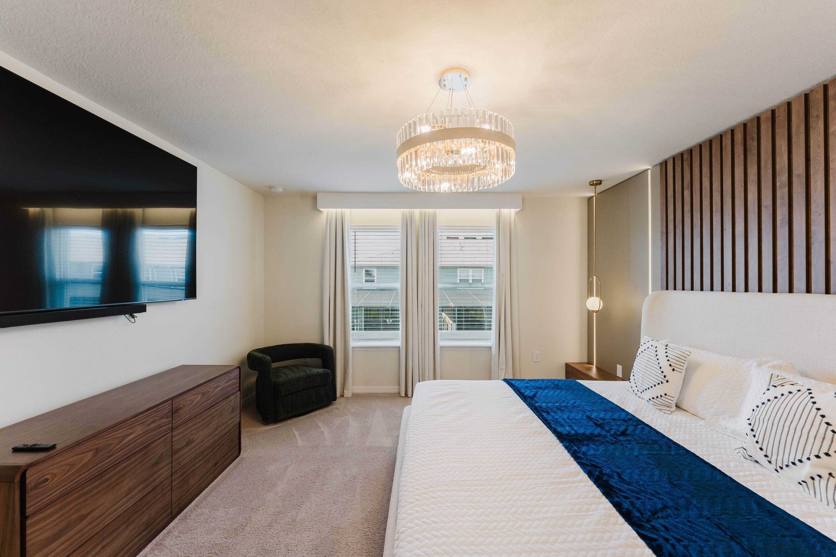 Une chambre moderne avec un grand lit, un téléviseur fixé au mur et un lustre.