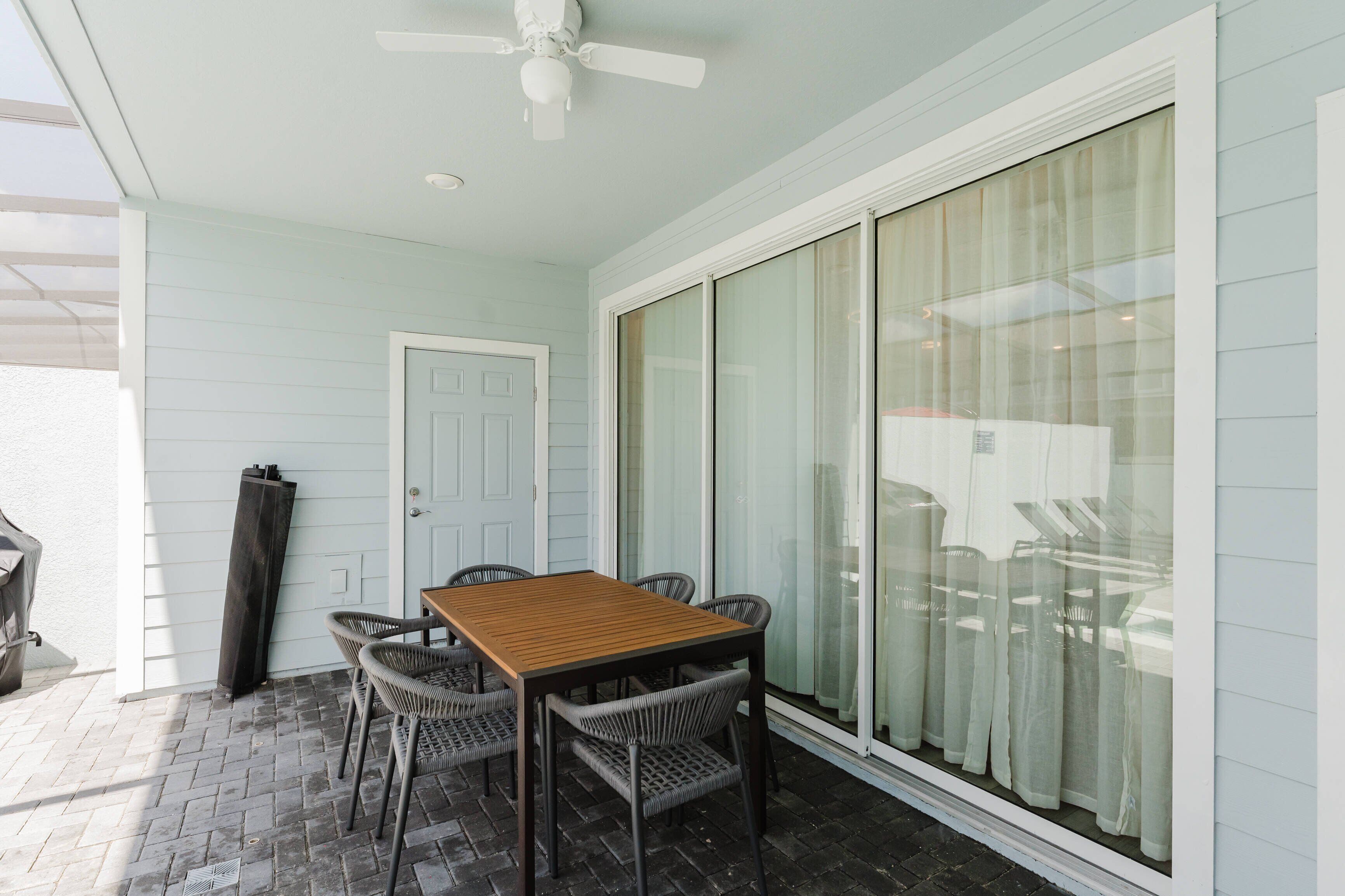 A covered patio with a table and chairs, a ceiling fan, and a sliding glass door.