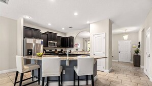 A modern kitchen with dark cabinets, a central island with bar stools, a microwave, and a refrigerator.