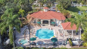 Ein Resort mit einem zentralen Schwimmbecken, mehreren Liegebereichen inklusive Sonnenschirmen und einem großen Gebäude mit rotem Ziegeldach.