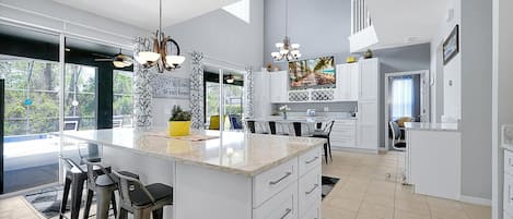 A modern kitchen with a large island, bar stools, and a dining area with a view of the outdoors.