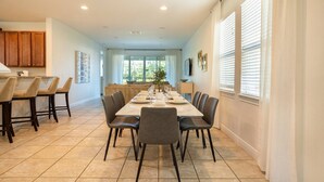 Un espace repas avec une longue table, des chaises et une cuisine en arrière-plan.