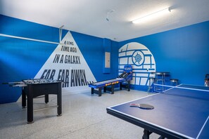 A room with a foosball table, ping pong table, and a wall with a space-themed mural.