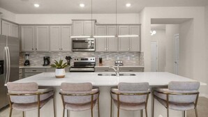 A modern kitchen with white cabinets, stainless steel appliances, and a central island with bar stools.