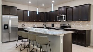 A modern kitchen with dark cabinets, stainless steel appliances, a central island with bar stools, and pendant lighting. - Last Minute Disney Getaway! Private Pool & Themed Bedrooms. Book Now! #136701 (Orlando)