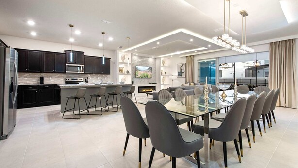 A modern kitchen with dark cabinets, a central island, and a dining area with a glass table and chairs. - Last Minute Disney Getaway! Private Pool & Themed Bedrooms. Book Now! #136701 (Orlando)