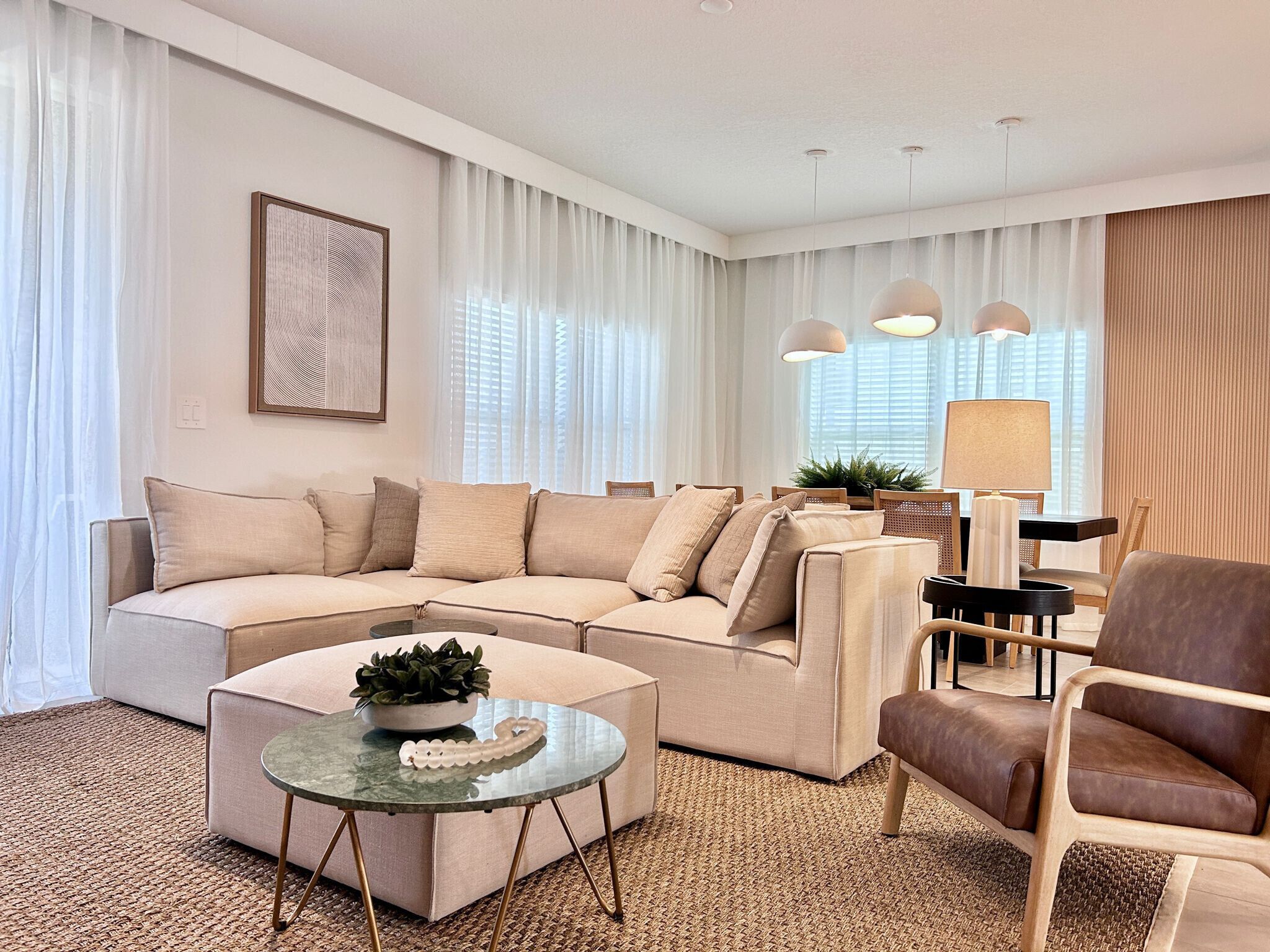 A modern living room with a sectional sofa, a glass coffee table, a brown armchair, and a lamp.