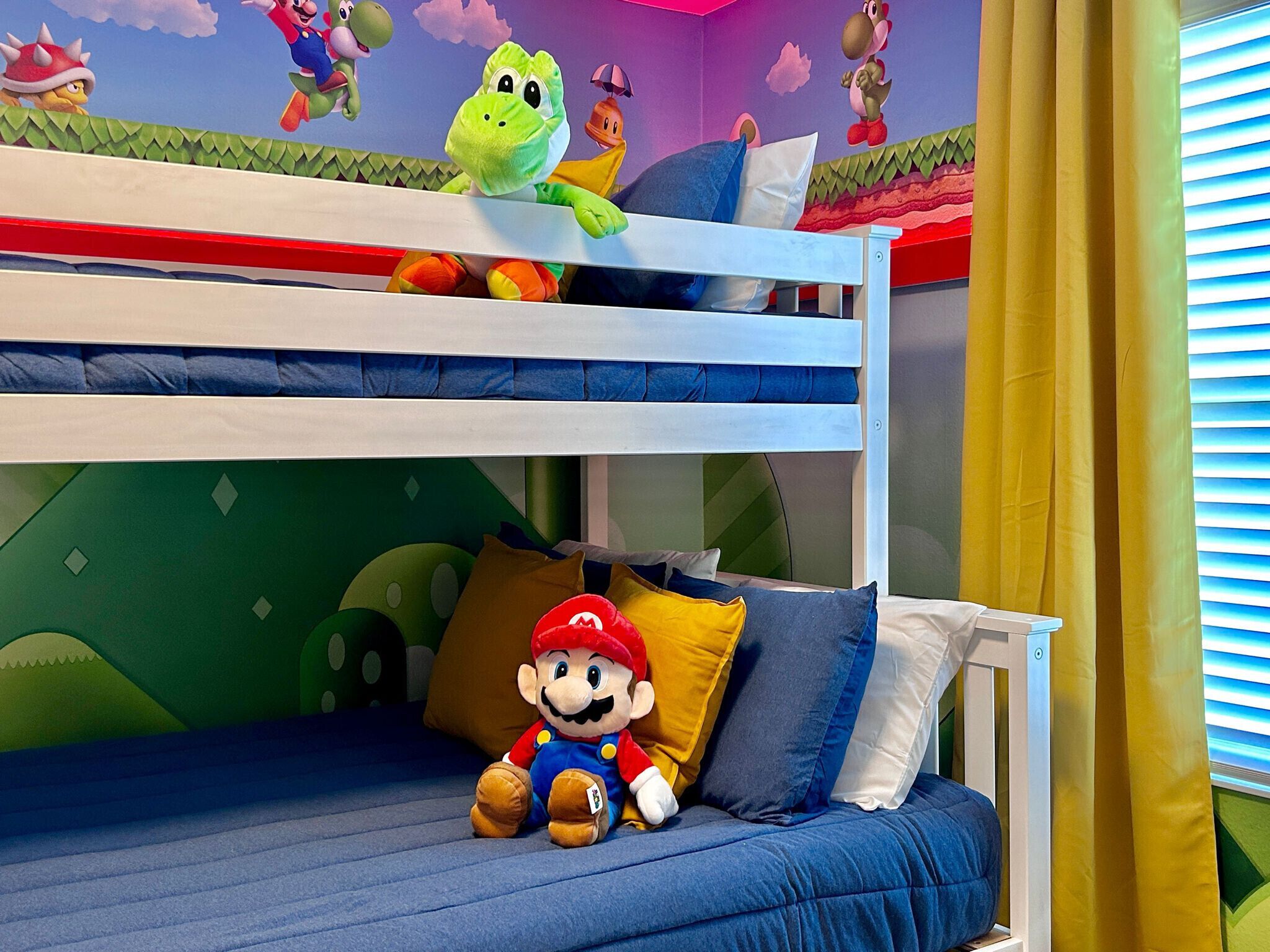 A bunk bed with a Mario plush toy on the lower bed, a green wall with Mario and Luigi characters, and a window with yellow curtains.