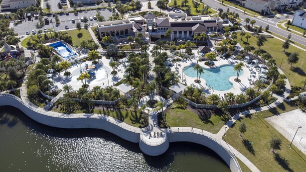 Vista aérea de un resort con una piscina central, un puente y un área ajardinada.