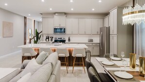 Una cocina moderna con armarios blancos, una isla central con taburetes de bar y un comedor con candelabro.