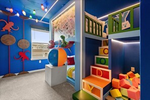 Una habitación infantil con una litera, estructuras de juego coloridas y un ventanal grande.