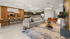 A modern kitchen with built-in appliances, a dining area with chairs, a living room with a sofa, and a decorative plant.