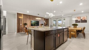 A modern kitchen with a large island, wooden accents, and a dining area with chairs and a table.