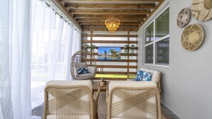A cozy seating area with wicker furniture, a wooden ceiling, and a view of a cityscape through a window.