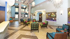 A spacious lobby with a high ceiling, wooden beams, and a mix of seating areas including armchairs and sofas.