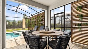 An outdoor patio with a round table and chairs, a pool, and a wooden wall with greenery. - Last Minute Disney Getaway! Private Pool, Game Room & Themed Bedrooms. Book Now! #147465 (Orlando)