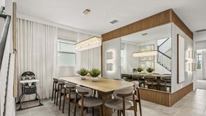A modern dining area with a large wooden table, multiple chairs, and a chandelier. There is a high ceiling with recessed lighting and a large mirror reflecting the room. - Last Minute Disney Getaway! Private Pool, Game Room & Themed Bedrooms. Book Now! #147465 (Orlando)