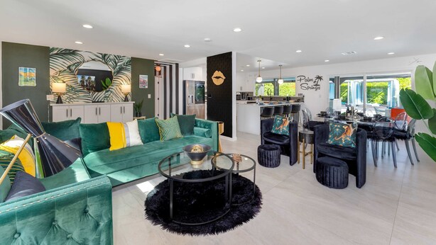 Een moderne woonkamer met een groene bank, een glazen salontafel en een eethoek met een zwarte eettafelset.