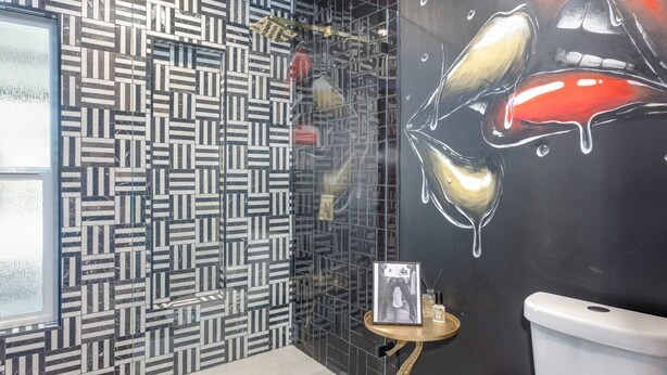 A bathroom with a patterned tile wall, a glass shower enclosure, a toilet, and a small table with a framed picture and a bottle. - Rat Pack Rendezvous - An Entertaining Experience (Palm Springs)