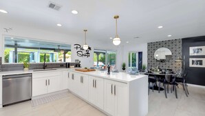 Een moderne keuken met witte kasten, een centraal eiland en hangende verlichting.