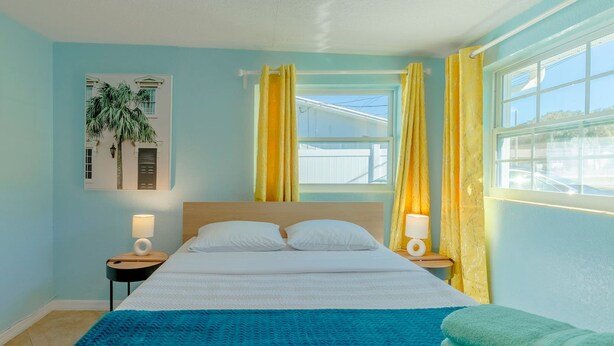 A bedroom with a bed, two bedside tables, a window with curtains, and a wall-mounted picture. - Tropical Paradise in Largo (Largo)