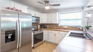 A modern kitchen with stainless steel appliances, white cabinets, a stone backsplash, and a large window providing natural light. - Tropical Paradise in Largo (Largo)