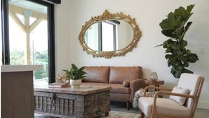 Ein Wohnzimmer mit einem rustikalen Couchtisch, einer Couch, einem Sessel, einem großen Spiegel und einem Topf mit Pflanze.