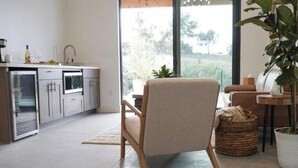 Eine moderne Küche mit integrierten Geräten, eine Essecke mit einem Stuhl und ein großes Fenster mit Blick ins Grüne.