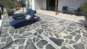 Ein überdachter Patio-Bereich mit Steinböden, einem Pool und Liegestühlen.