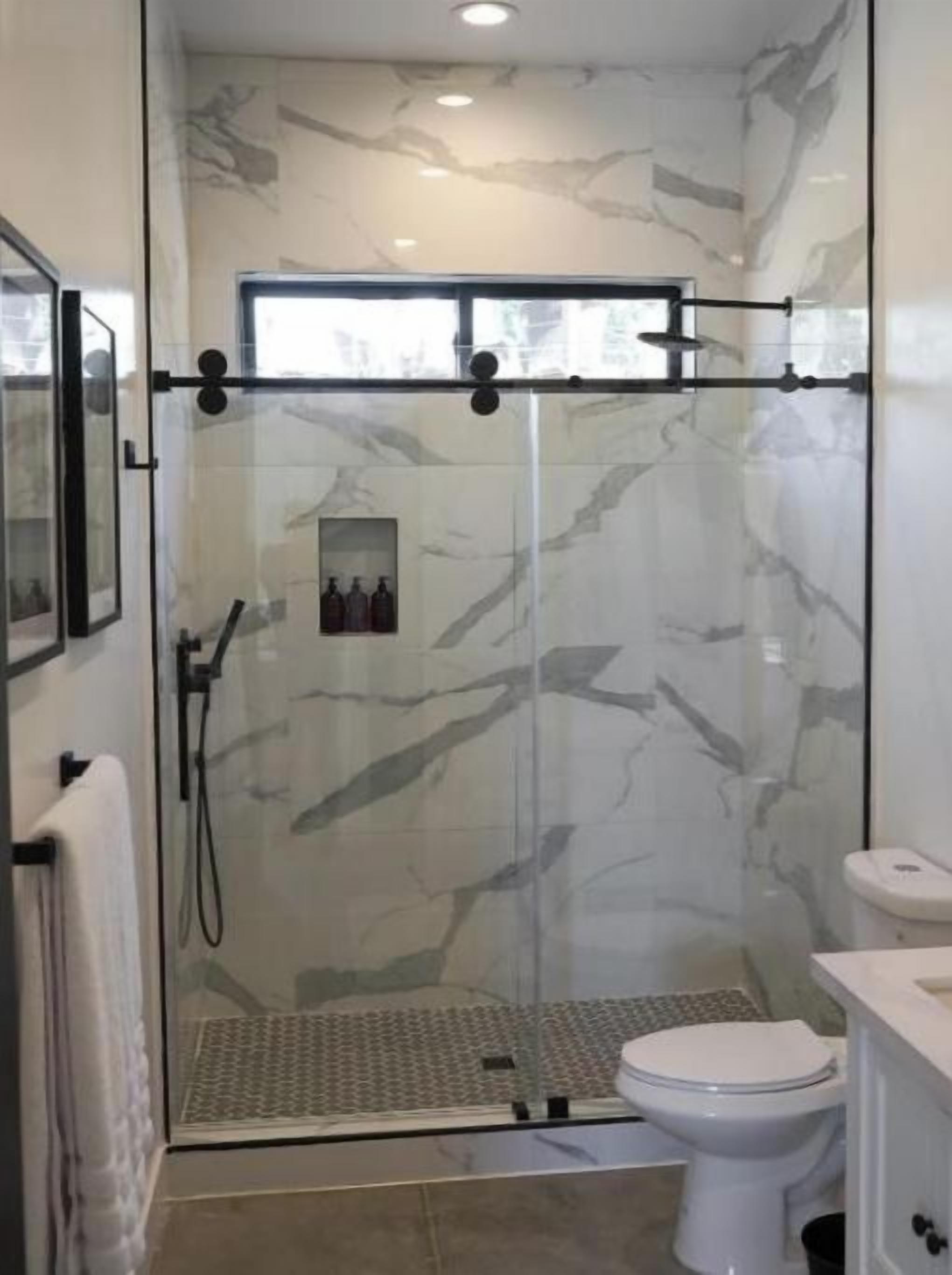 A modern bathroom with a glass-enclosed shower, a white toilet, and marble-patterned walls.