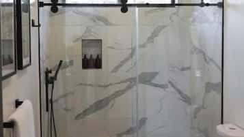 A modern bathroom with a glass-enclosed shower, a white toilet, and marble-patterned walls.