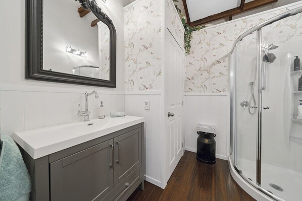 A bathroom with a vanity, a mirror, a shower enclosure, and floral wallpaper. - Fisherman Cottage - Waikanae Beach (Waikanae Beach)
