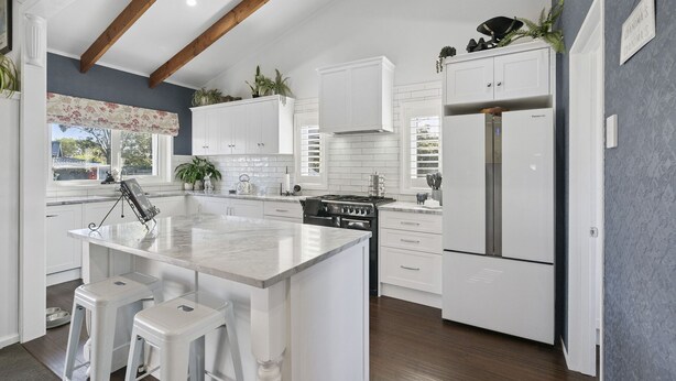 Une cuisine moderne avec des meubles blancs, un îlot central doté de tabourets, une cuisinière encastrée et un réfrigérateur.