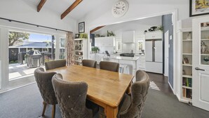 Un coin repas avec une table en bois et des chaises rembourrées, une cuisine avec des meubles blancs et des appareils électroménagers, et une horloge au mur.
