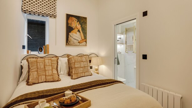 Une chambre d’hôtel avec un grand lit, un plateau avec des articles pour le petit-déjeuner, un tableau au mur et une fenêtre donnant sur un beau paysage.