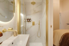 Ein modernes Badezimmer mit Marmorwand, goldener Dusche und Waschbecken in Weiß.