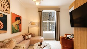 Un salon moderne avec un canapé, une table basse ronde, un lampadaire et une vue sur un bâtiment en briques, visible à travers une fenêtre.
