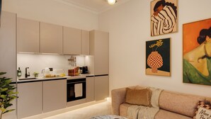 Une cuisine moderne équipée d’un four encastré, d’une machine à café et d’un évier. On y trouve un canapé beige avec un plaid et un coussin. Une plante en pot est placée sur le côté gauche.