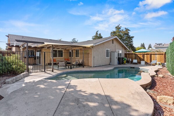 A residential backyard with a swimming pool, a covered patio, and a wooden fence. - Citrus Retreat with Pool (Citrus Heights)