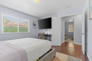 A bedroom with a bed, a desk, a television, and a door leading to another room. - Citrus Retreat with Pool (Citrus Heights)