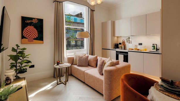 A modern living room with a sofa, a round side table, and a plant. - Notting Hill | 1-Bedroom Deluxe Apartment (London)