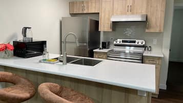 A modern kitchen with a stainless steel refrigerator, oven, and microwave. There is a sink with a faucet, and wooden cabinets above.