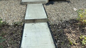 Una casa con revestimiento gris, una puerta principal blanca con el número 7949 y un pequeño porche de madera con escalones que conducen a la puerta.